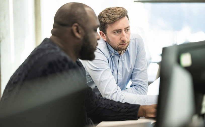 Two professionals collaborate at a desk during a consultation focused on payments optimisation, reviewing information on a computer screen 